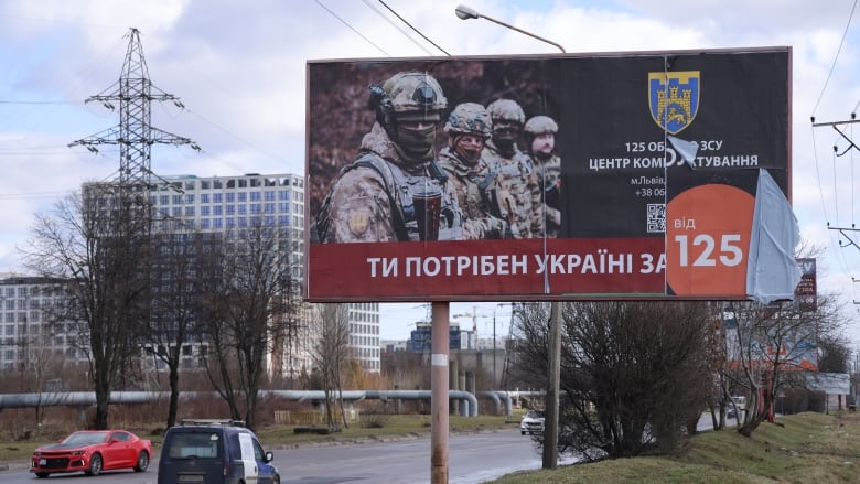 A billboard with four soldiers on it stands near a road with cars on it.