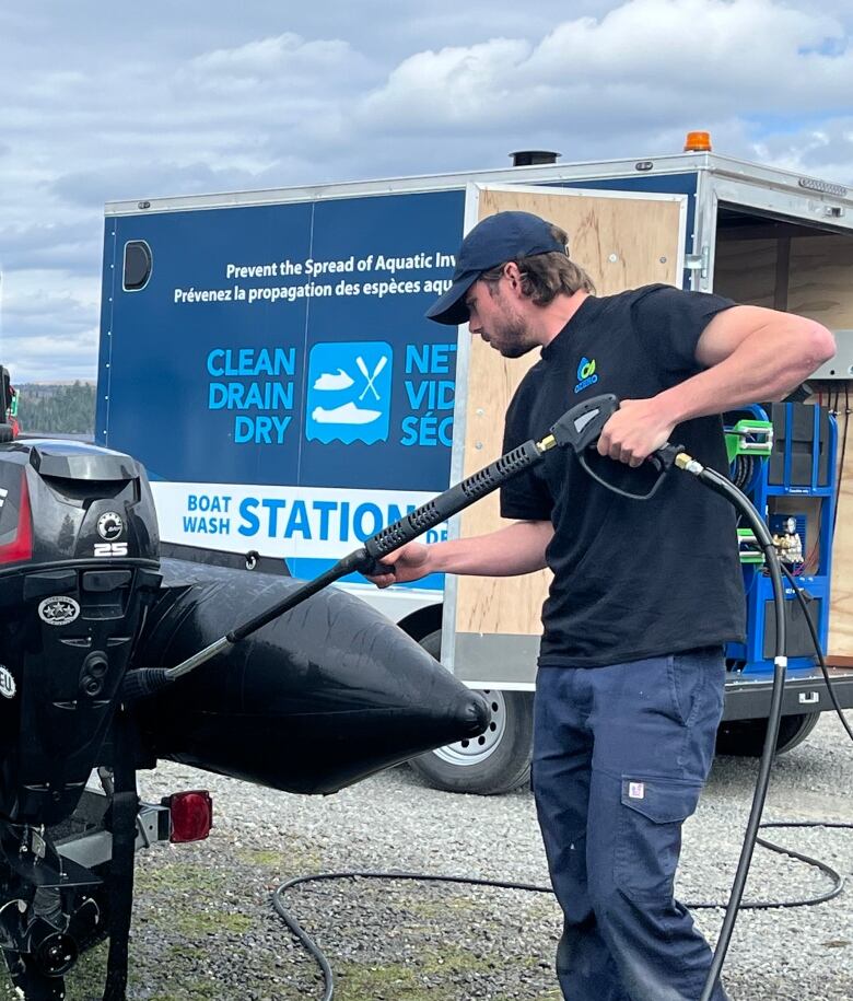 A man with a power sprayer washes of a small boat with a motor.