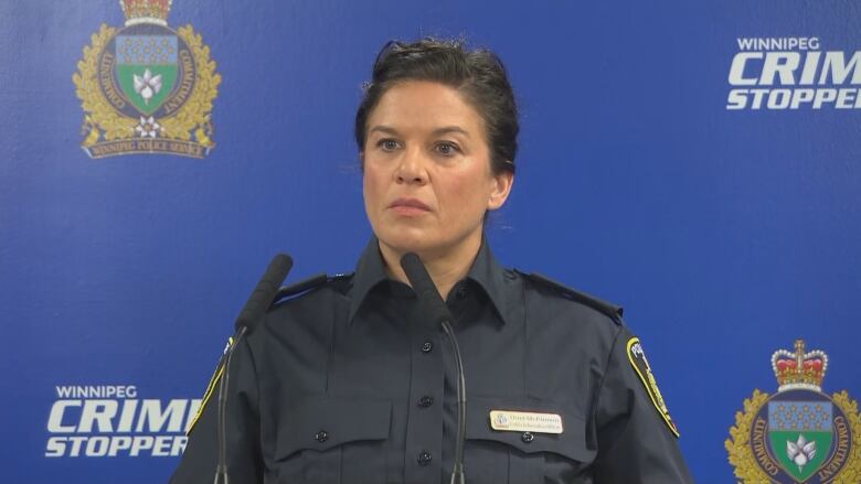 A police officer in uniform stands in front of microphones.