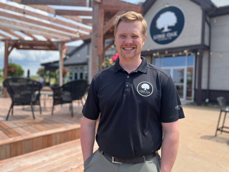 A man stands in front of a pub, with outdoor seating in the background. 