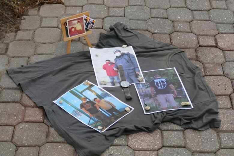 A shirt lays on the ground, covered with pictures and a watch.