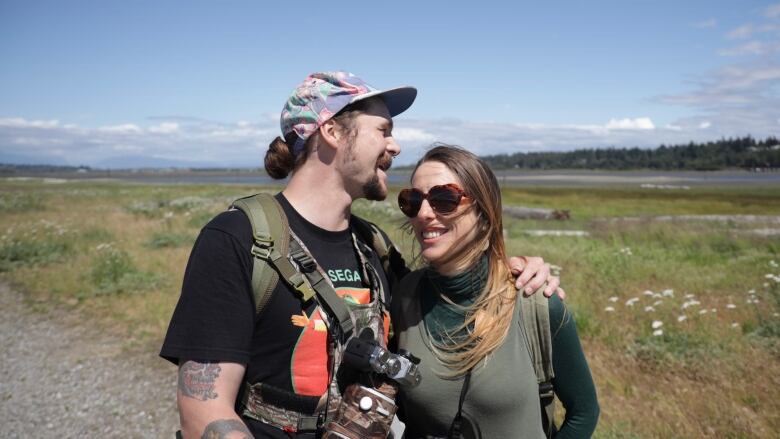 A man and woman in the sunshine with wilderness tidal area behind them