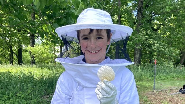 A child holds honeycomb while wearing a beekeeping suit