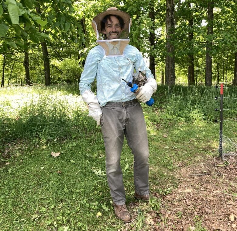 A man smiles while wearing a beekeeping hat.