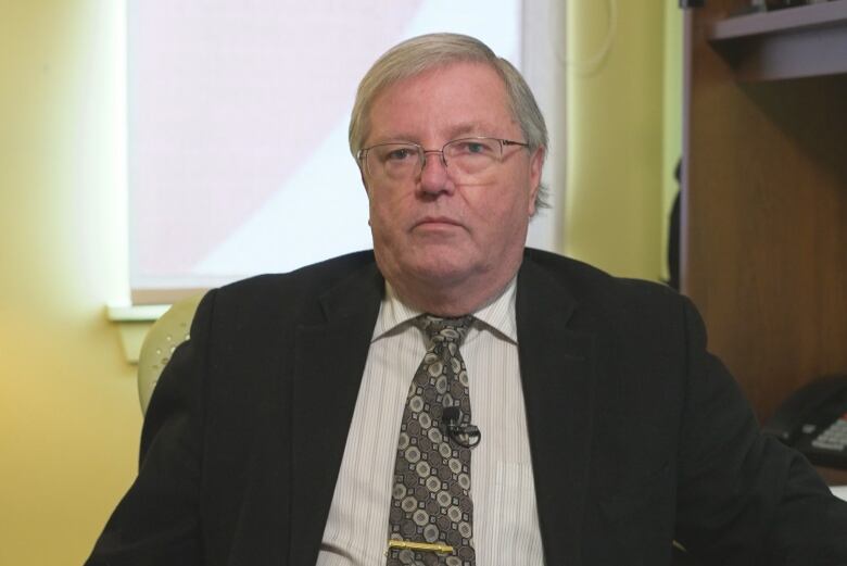 A man wearing glasses in a dark suit looks at the camera.