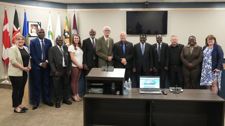 A group of men and women in business wear pose in a room with a kenyan and canadian flag to their left behind them