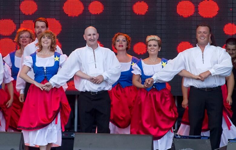 An Acadian dance troop wearing outfits with white, red and blue colours performs.