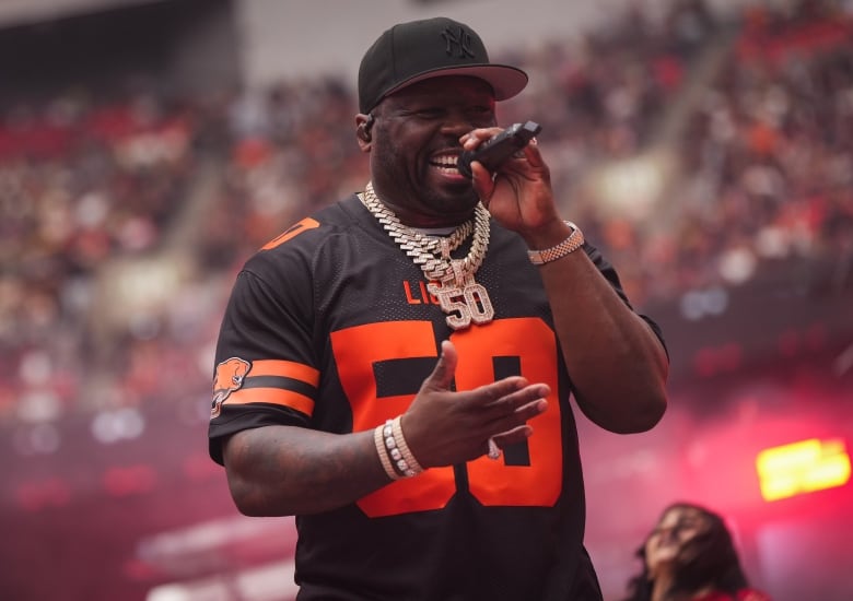 a man in a black baseball cap sings into a microphone and smiles