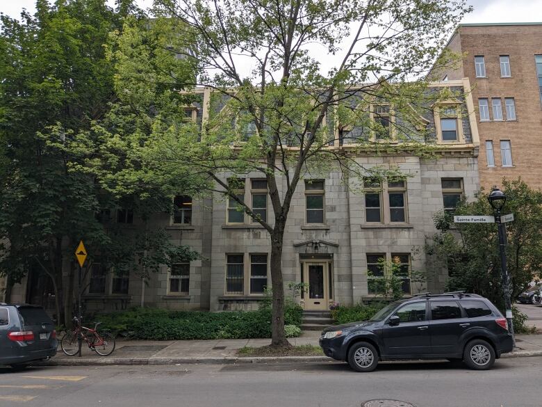 The exterior of a building on a street with trees and cars. 