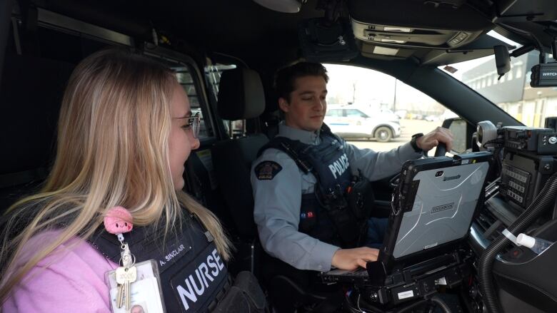 A nurse and RCMP officer sitting in an RCMP vehicle working. 