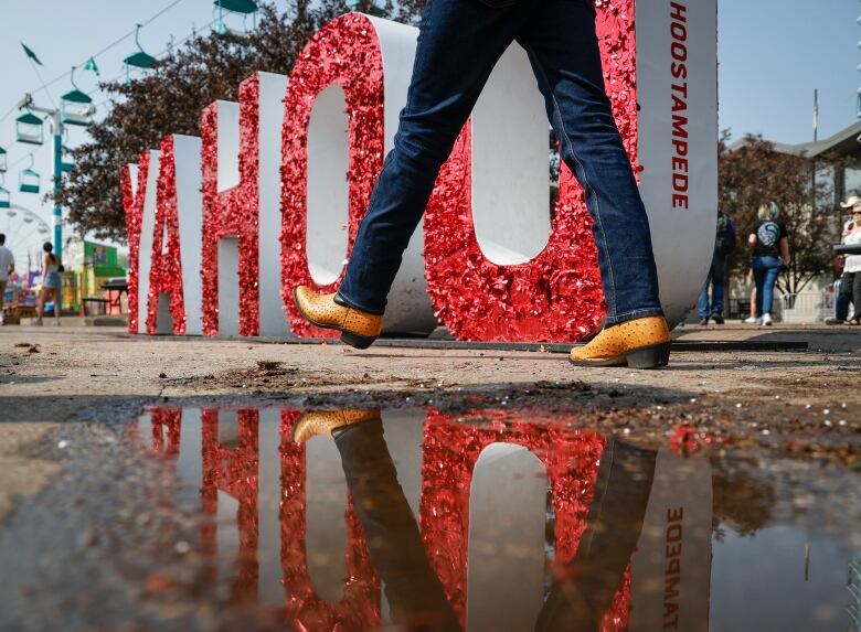 cowboy boots reflected in a puddle, with a large YAHOO sign in the background.