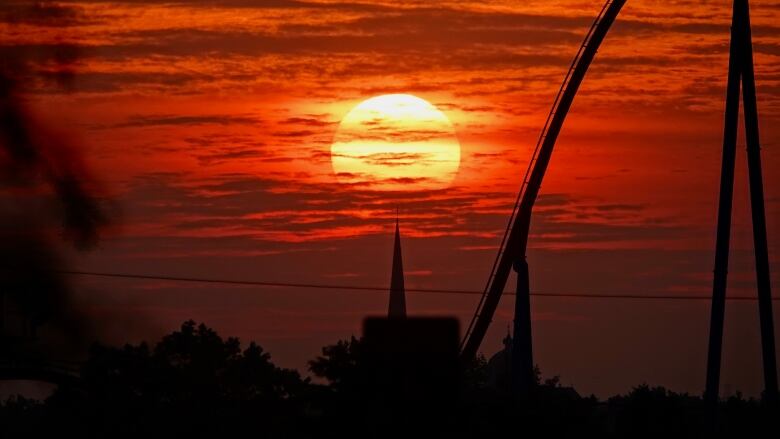 A close-up shot of the sunrise peaking through clouds with the shadow of a rollercoaster. 