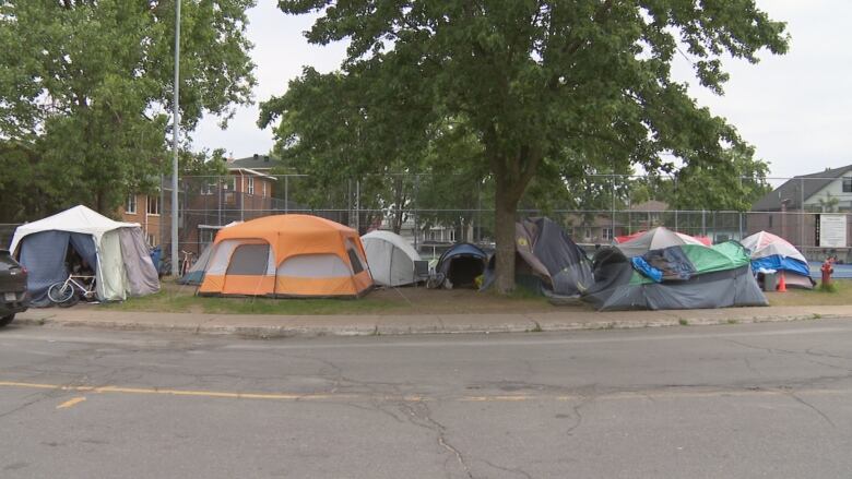 Many tents set up against the fence of a tennis court. 