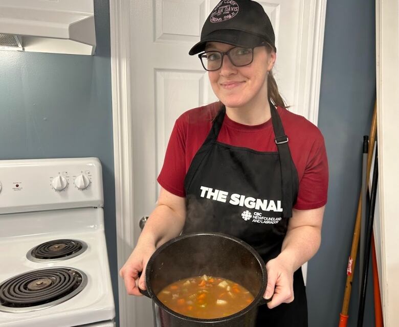 A woman with a hat and glasses stands in a kitchen .