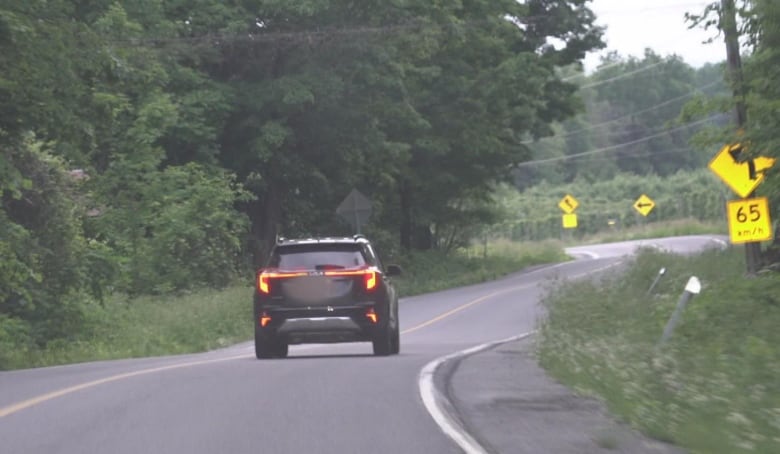 A black Kia speeds down a road.