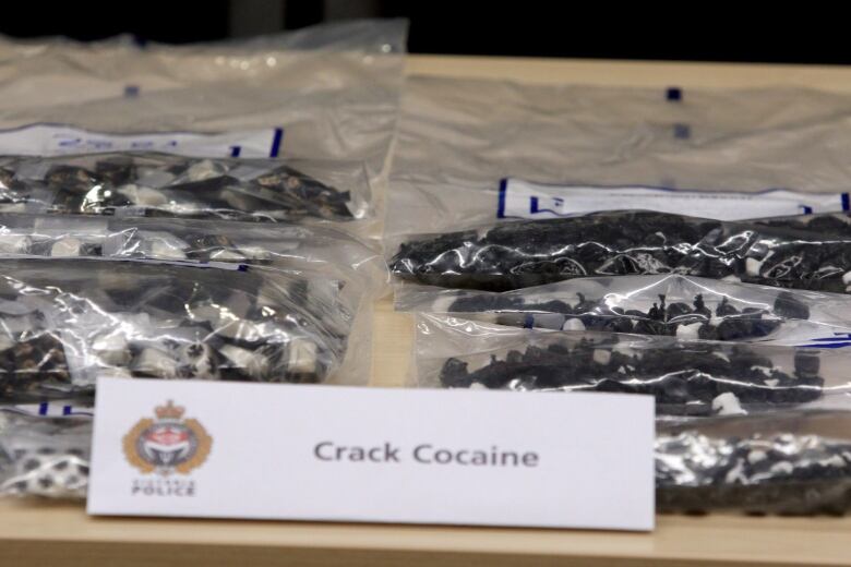 Multiple plastic bags with small black items inside of them. A sign on the table reads 'Crack cocaine'.