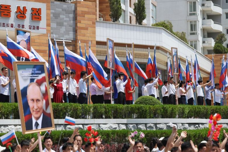 Asiatic people are seen on the side of what appears to be a parade route, holding large flags and waving banners. A portrait of an older Caucasian man is shown.