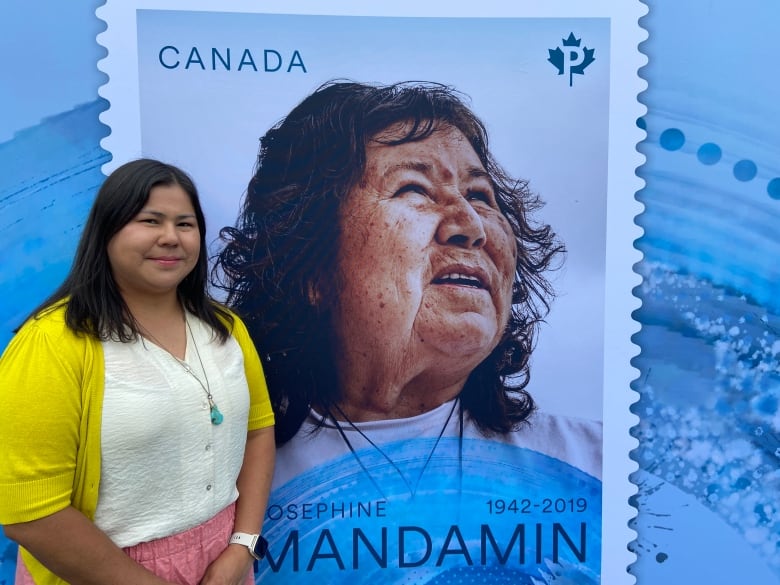 A woman stands in front of poster of unveiled postage stamp. 