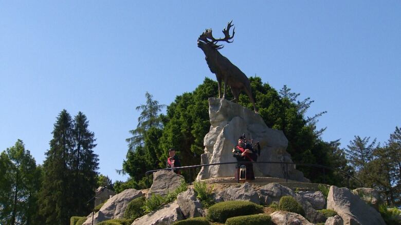 Two man stand beneath a statue of a caribou. 