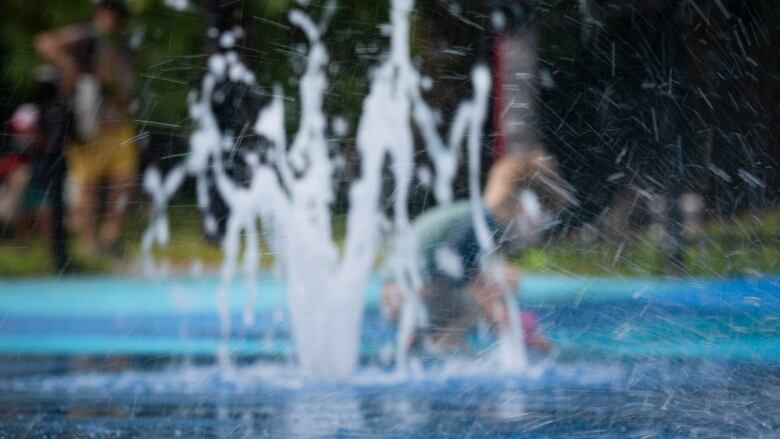 A child is seen through the mist playing in a splash park