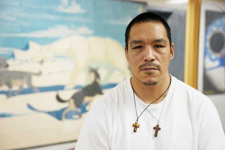 A man in a white t-shirt stands in a prison visitation room. 