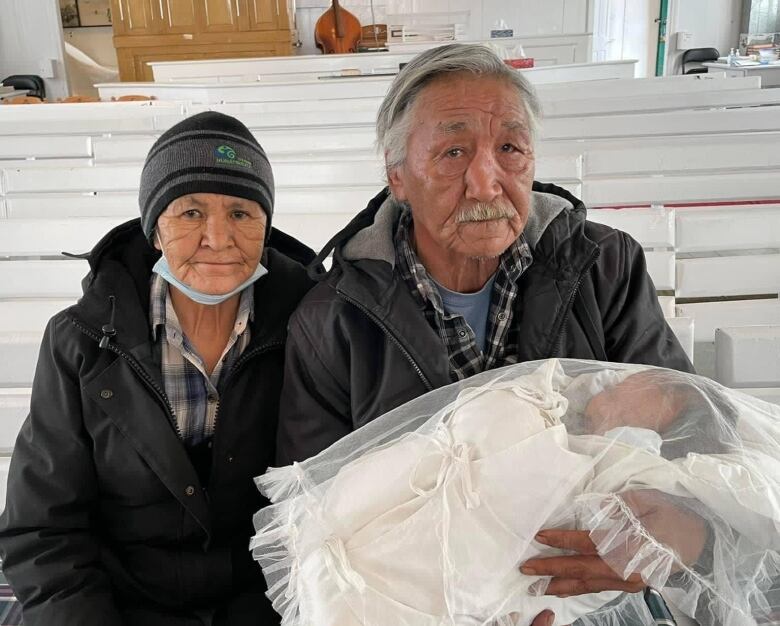 Two seniors sit on a white church bench. 