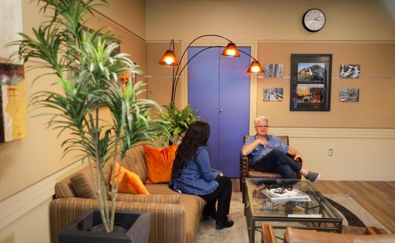 Ken Popove, the mayor of Chilliwack wears a purple shirt sits on a couch across from a CBC News journalist Baneet Braich in his office. 