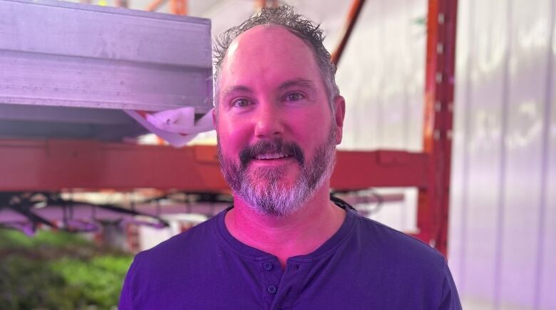 A smiling man with grey hair and beard wears a blue shirt.