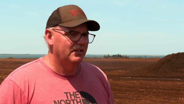 A man in a t-shirt and baseball cap stands in a field.