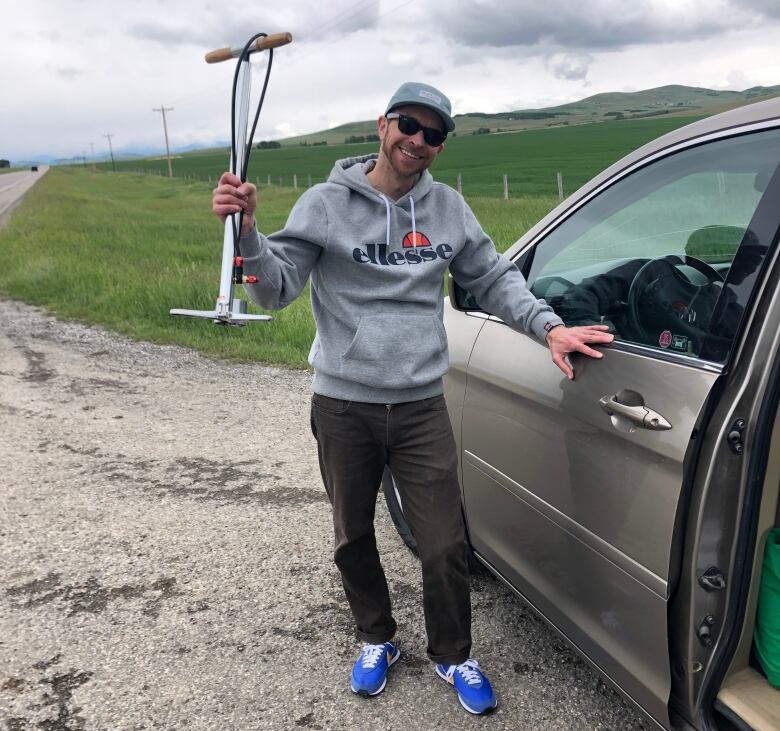 A man wearing a hoodie stands beside a minivan with a bike pump in his hand.