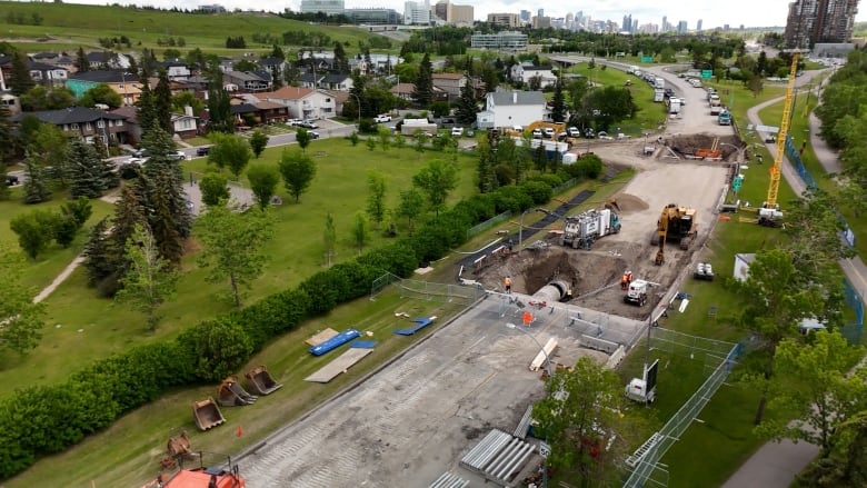 a large open excavation site with heavy duty construction equipment and workers working on a large exposed underground pipe.