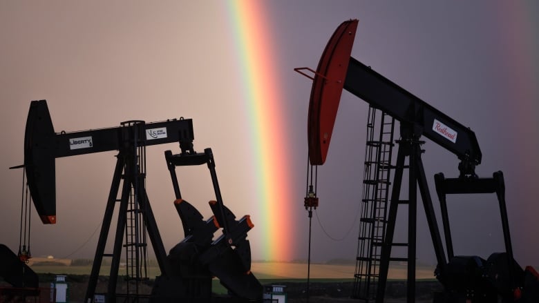 A rainbow between the silhouettes of two oil wells. 