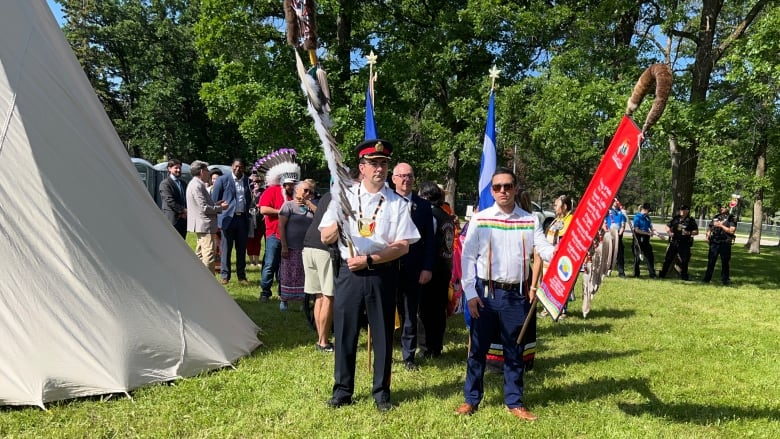 A line of people holding flags and signs walk past a teepee.