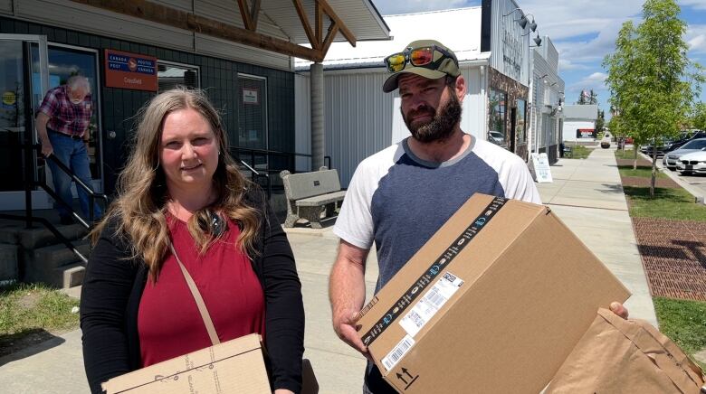 A couple stands outside the post office in Crossfield. They're carrying several large parcels.