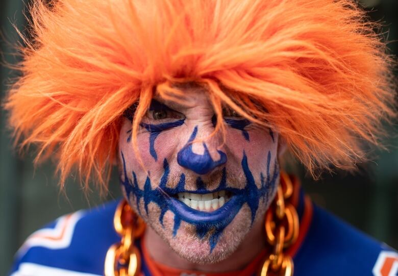 A close up of a man with Orange hair and blue face paint grimacing. 