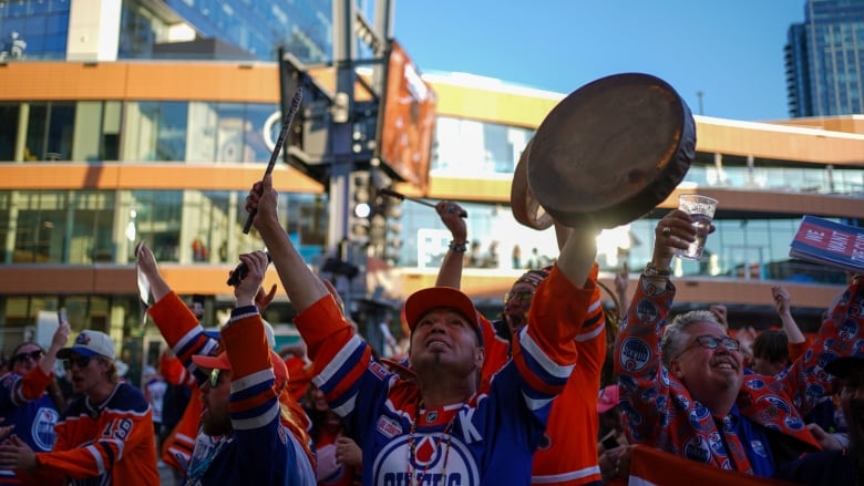 A group of people in blue and orange raise their hands smiling. 