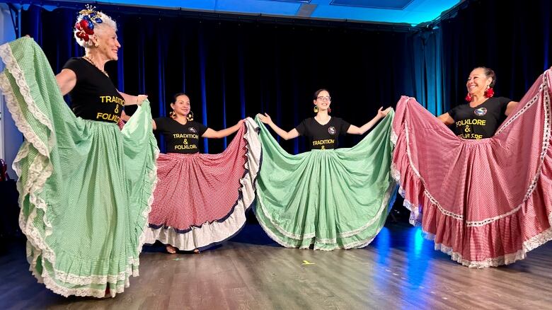 Four women in red and green skirts lift the sides of their skirts to show them off.