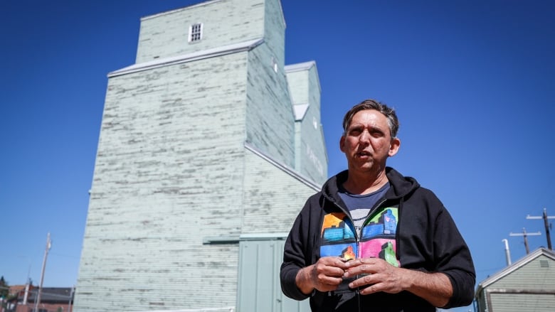 A man stands in front of an old grain elevator.