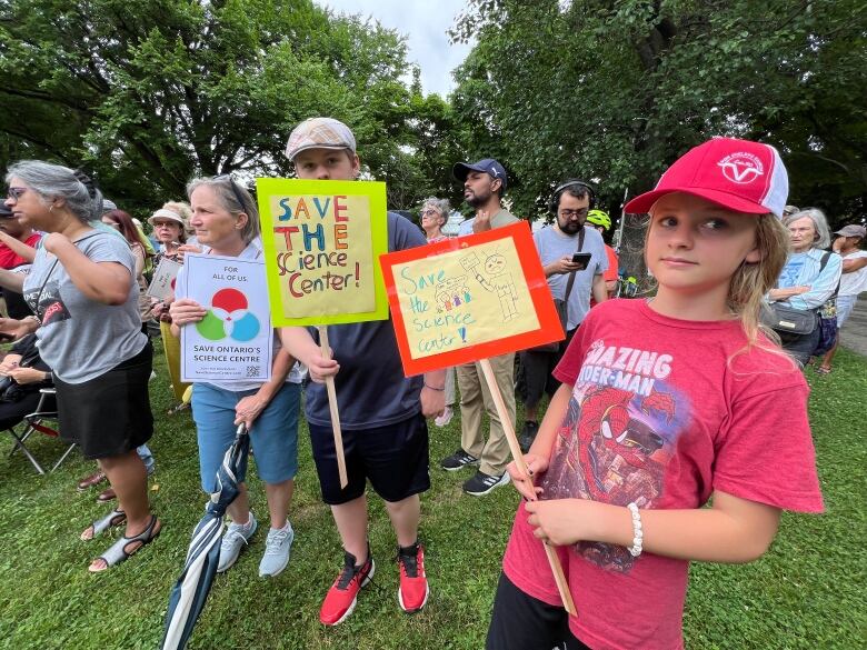 Two children are among a group of people at a rally in a park.