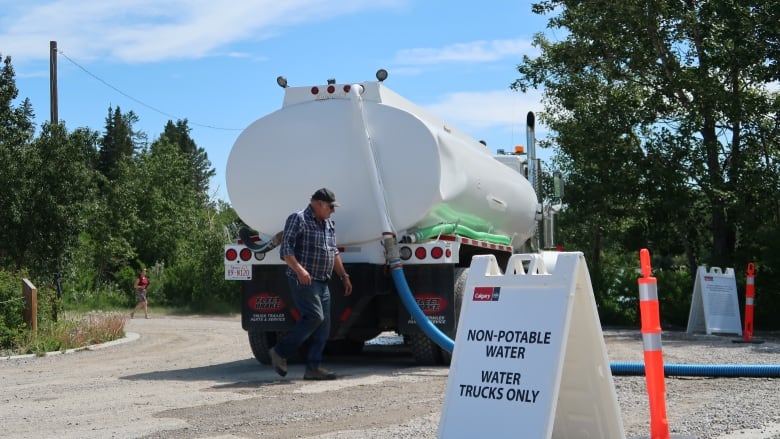 A man walks around the back of a water truck.