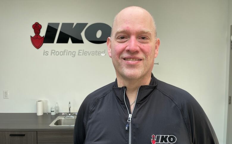 A man stands in front of a sign for IKO Industries.