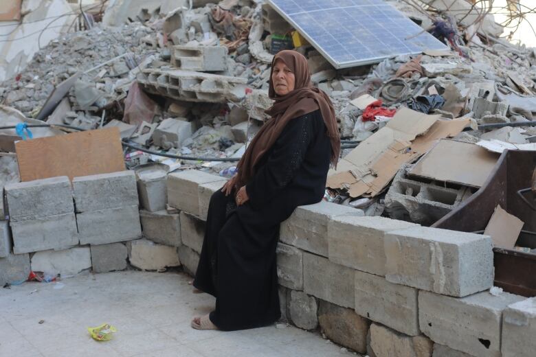 A woman sits on concrete in front of a pile of rubble.