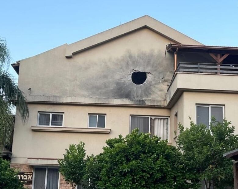 A home is seen with a large, round hole puncturing a wall on the top floor. 