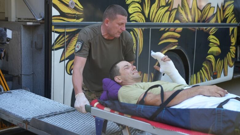 A man in a green shirt with a bandaged left arm on a stretcher is loaded into a vehicle by another man.