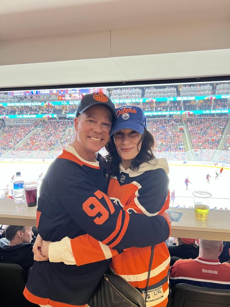 A couple in matching jerseys hug each other in a hockey rink.