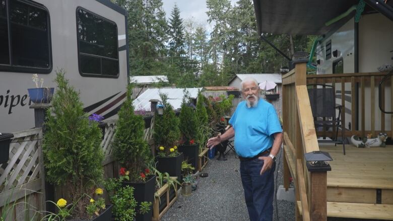 A man in a blue t-shirt shows off potted plants next to an RV.