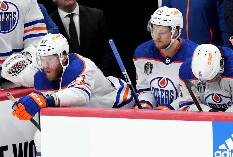 Three male ice hockey players appear dejected while sitting on their team's bench.