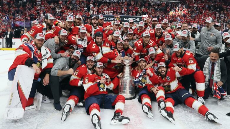 A male ice hockey team poses for a group picture on the ice around the Stanley Cup.