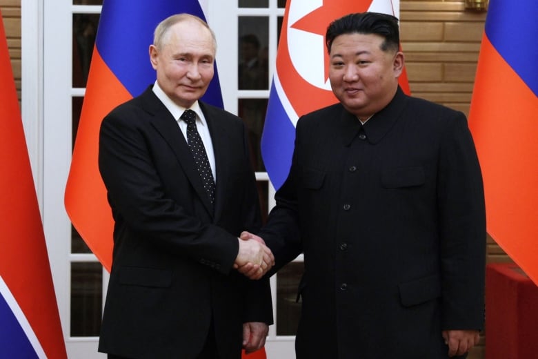 Russian President Vladimir Putin shakes hands with North Korea's leader Kim Jong in front of their country's flags during Putin's visit.