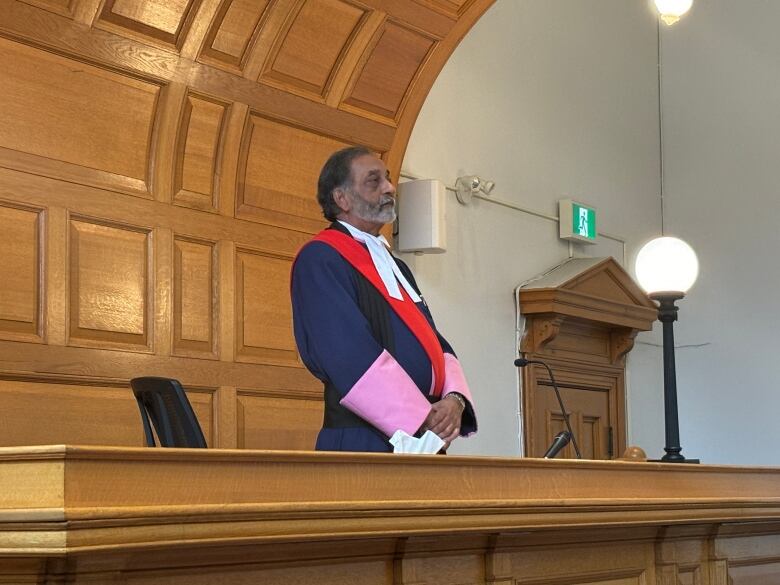 A man in judge's robes standing in front of a courtroom.